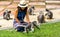 Woman in sarong and whit fedora sitting on ground surrounded by dusky monkeys