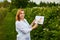 Woman scientist working in fruit garden and shows the level of crop growth using infographics. Biologist inspector examines blackb