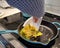 Woman scrambling eggs using a piece of a plastic plate as a spatula