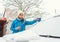 Woman scraping off ice from front window of her car in winter