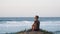 Woman seated by the ocean at sunset, enjoying views of waves.