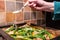 Woman seen sprinkling sesame seeds onto a nearly prepared breast of chicken and asparagus meal.