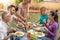 Woman serves the food with friends happy around the table.