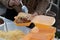 Woman serving jacket potato and its toppings into a take away lunch box.