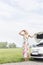 Woman shielding eyes while standing by broken down car on country road