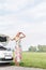 Woman shielding eyes while standing by broken down car on country road