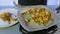 A woman shifts fried chicken with green beans and mushrooms from a frying pan into a white plate