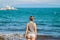 Woman in shirt and shorts on beach. Bright photo of young girl watching cruise boat.