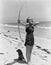 Woman shooting bow and arrow on beach