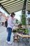 Woman shopping choosing pot with plant in store, on an outdoor rack