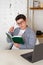 Woman with short black hair in glasses sits attentively at table, making notes in notebook. Planning, budgeting