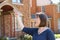 Woman with short hair in front of blurred brick houses points and looks surprised