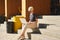 Woman with short hair working on laptop, screen space for design layout. Sitting outside at stairs, sunny day, caucasian type.