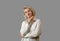 Woman with short white curly hair is wearing a sloppy white shirt. Holds his hand to his face. Studio shot of beautiful woman