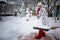 A woman with a shovel clears snow from the tile area. The girl cleans the snow in the yard. Snow cover on the knee. in red felt