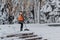 Woman with a shovel in an orange waistcoat cleans snow