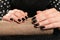 Woman showing black manicure on rolled shiny paper, closeup. Nail polish trends