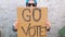 Woman shows cardboard with Go Vote sign on brick wall urban background. Honest political voting concept. Use your voice