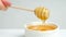 A woman shows liquid linden honey in a ceramic white bowl, mixes honey with a wooden spoon