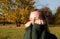 A woman is shy of the camera, hides face in the collar of a green sweater, background of autumn park