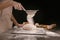 Woman sifting flour on dough against dark background