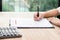 Woman signing on confidential contract with calculator on wooden