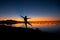 Woman silhouette on sunset beach. Tropical seaside landscape with happy tourist dancing. Bright orange and blue sky