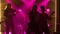 Woman singer performs with rock music band in dark studio with purple lights. Silhouettes of people playing electric and