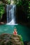 Woman sit on rock under waterfall in tropical jungle