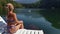 Woman sit on a sunbed in sunglasses and swimming suit. Girl rest on a flood wood underwater pier. Ducks and swans are