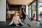 Woman sits at easy pose while her husband vacuums floor with baby riding on neck