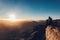 Woman sits on edge of cliff on Mount Sinai against background of sunrise.