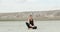 A woman sits in the lotus position on dry ground against the backdrop of a hill