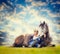 Woman sits at lying horse and looking outside over pasture background