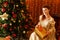 Woman sits near  Christmas tree and holds a gift on the background of garlands.