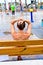 A woman sits on a wooden bench with her arms on her head as she watches children at a splash park