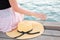 A woman sits on a wooden pier and reaches for a straw hat. Hand and hat close-up. The sea in the background. The concept of summer