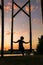 A woman sits on a wooden swing against the backdrop of sunset in Kyiv