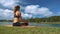 Woman Sits in Yoga Pose on Lake Shore under Sky