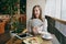 Woman sitting alone in coffee shop at table with bundle of dollars, cash money, cup of cappuccino, cake, relaxing in