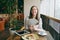 Woman sitting alone in coffee shop at table with bundle of dollars, cash money, cup of cappuccino, cake, relaxing in