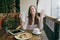 Woman sitting alone in coffee shop at table with bundle of dollars, cash money, cup of cappuccino, cake, relaxing in