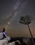 Woman sitting alone on top of huge boulder under dark starry summer sky enjoying mountain quietness