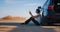 Woman sitting aside of breakdown vehicle with warning triangle emergency lights