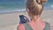 Woman sitting on beach and texting on smart phone