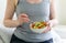 Woman sitting on the bed and holds bowl with vegetable salad