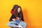 Woman sitting behind gaming chair in her hands holding red gamepad on yellow background