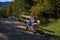 Woman sitting on the bench enjoys the warm rays of the sun on a hiking trail in the forest in autumn. Feeling freedom