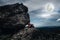 Woman sitting on boulders, sky with cloudy and full moon. Low key and high contrast style.