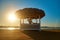 Woman sitting at Cabana with straw roof on a sandy beach on sunset